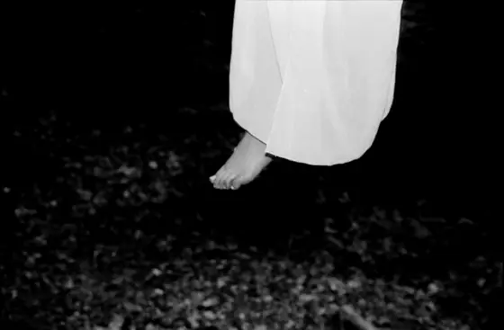 Bare feet dangling above the ground, partially covered by a long white dress, in a black and white photo taken at night.