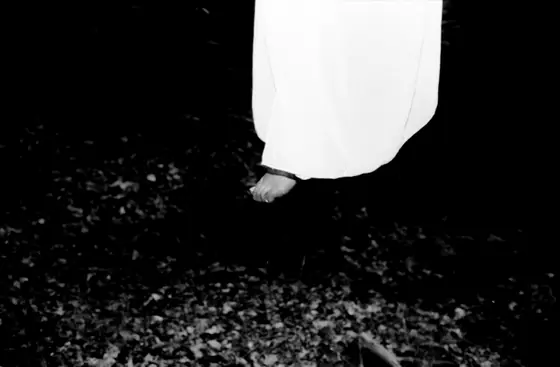Bare feet hanging above ground covered in leaves, with a white garment visible from the knees down.